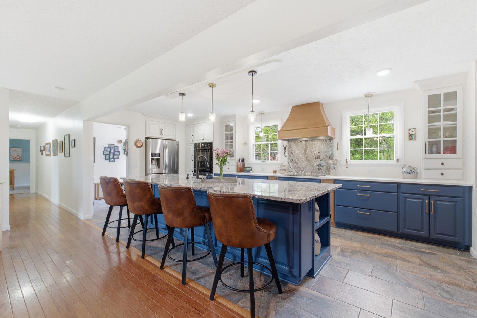 Updated kitchen with a large granite island, blue cabinetry, and copper hood