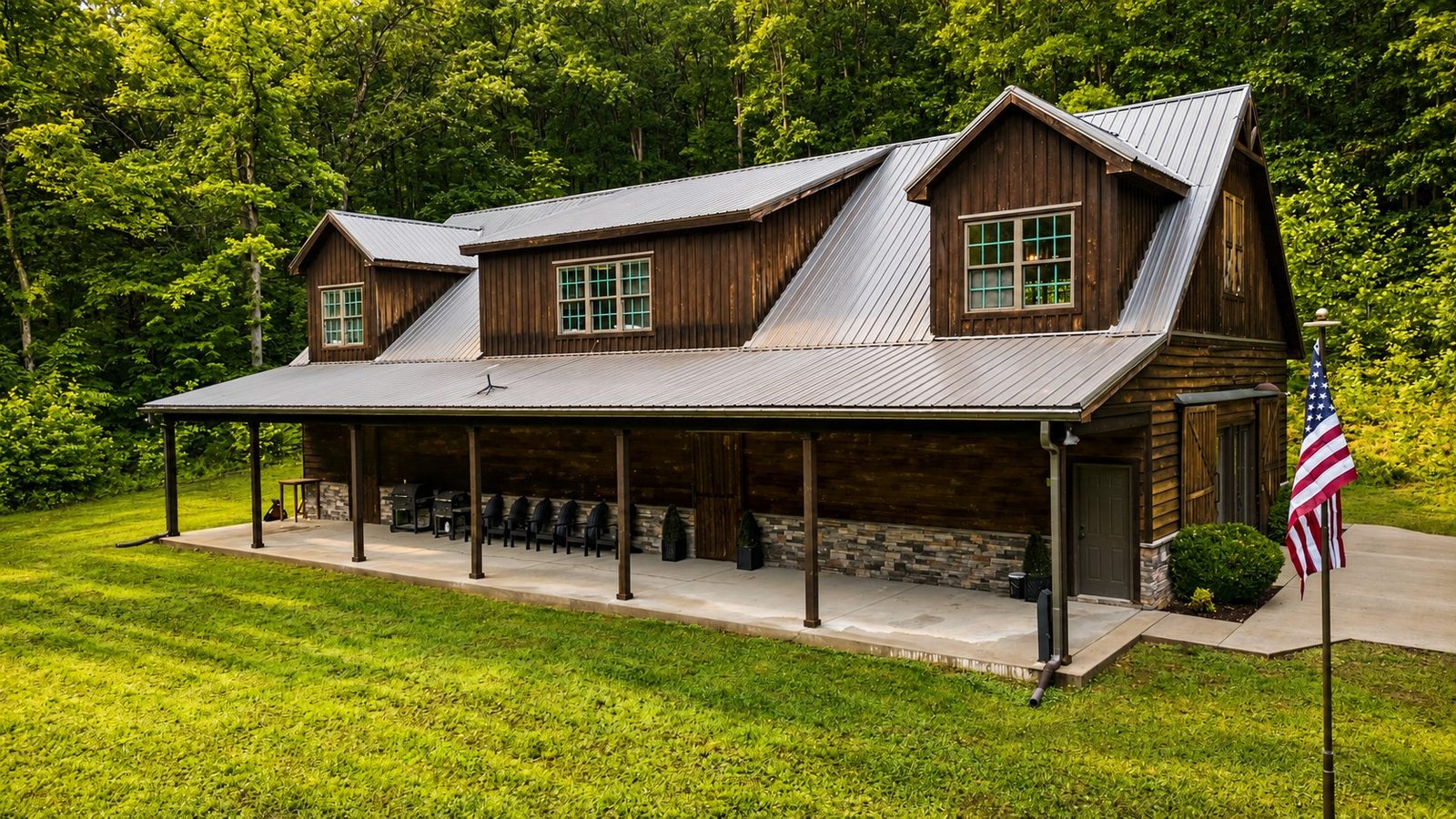 The barndominium with its metal roof and wraparound porch at the edge of the woods