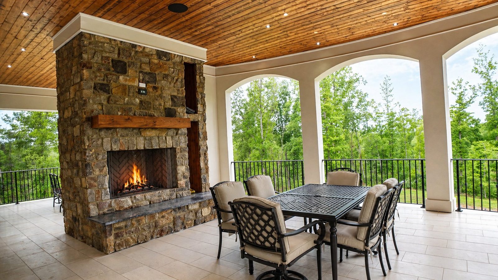 Covered outdoor entertaining space with stone fireplace and arched colonnade